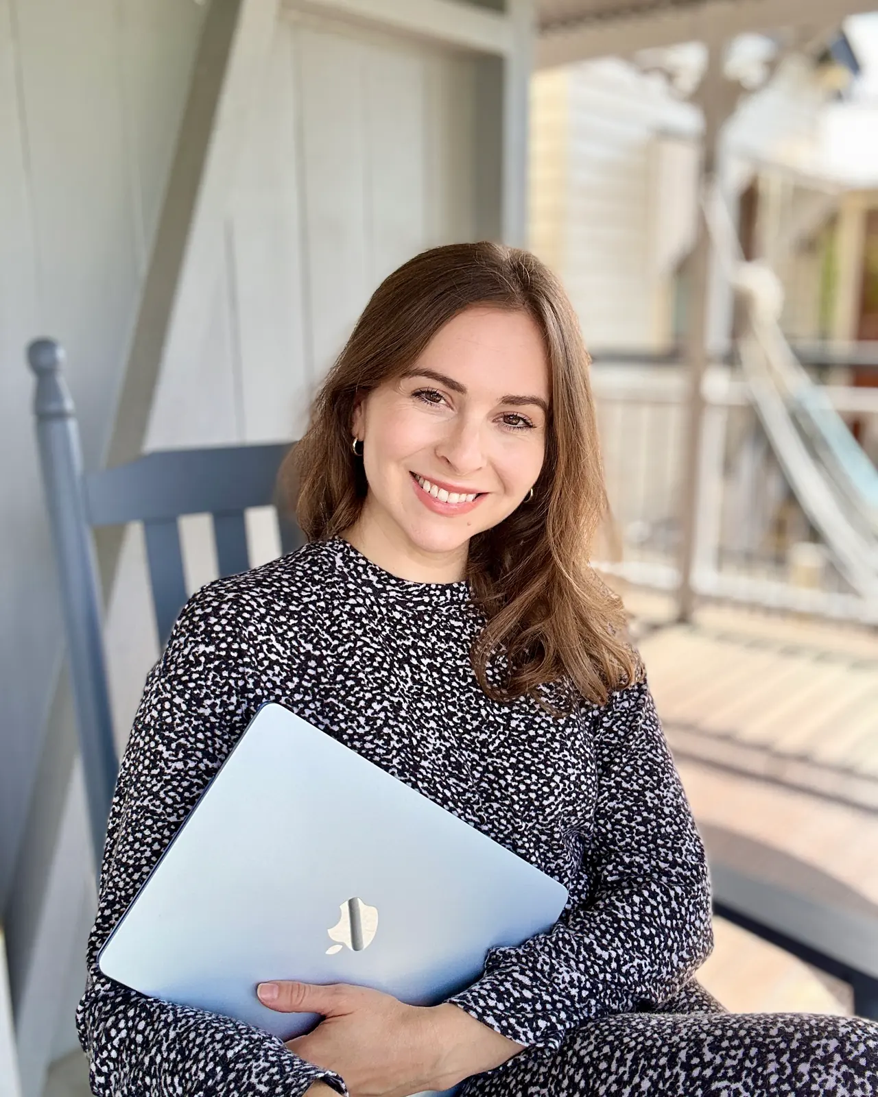 Lex in Wonderland smiling on a porch chair with a laptop on her lap