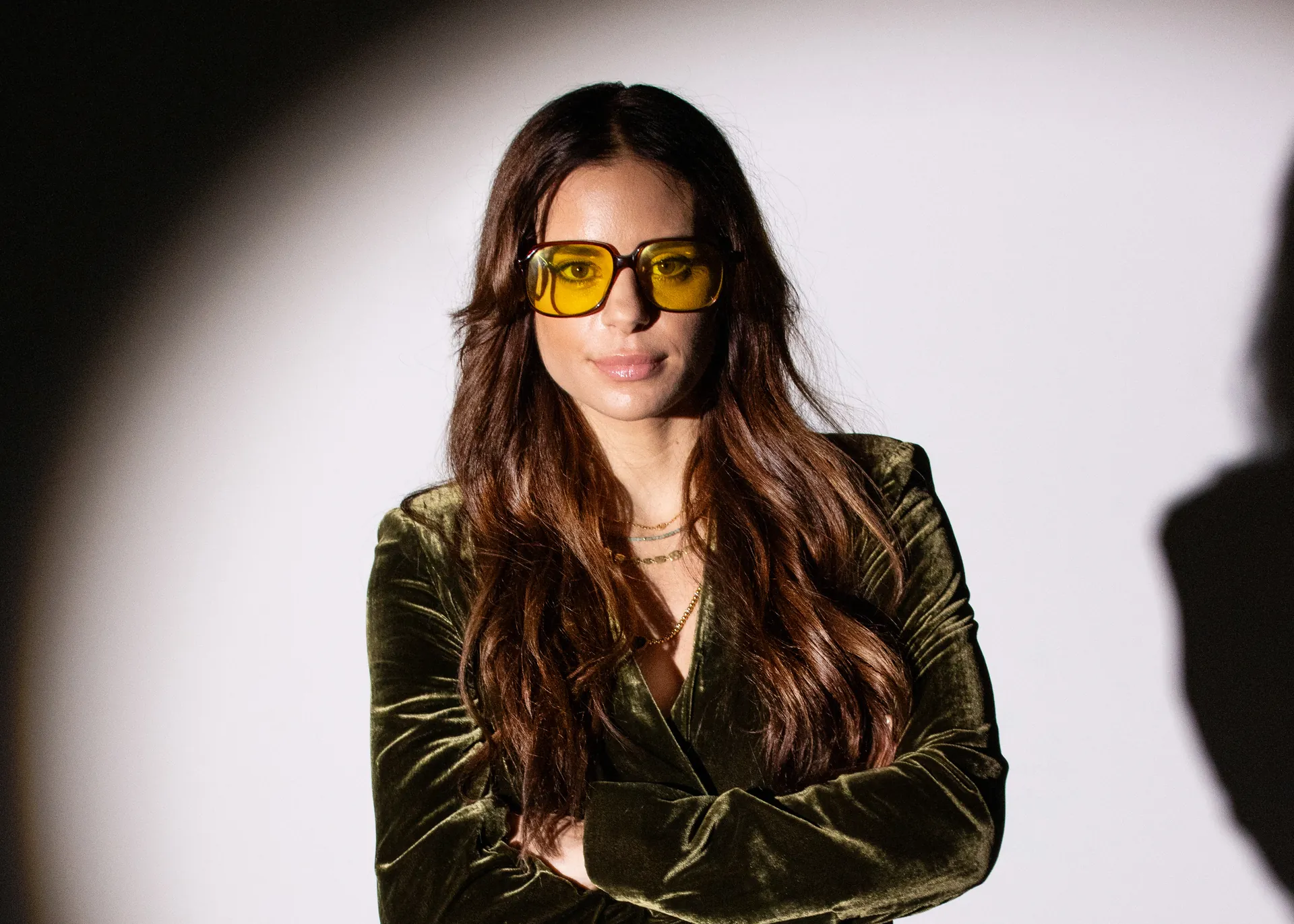 Poppy Reid in yellow-tinted glasses, arms folded