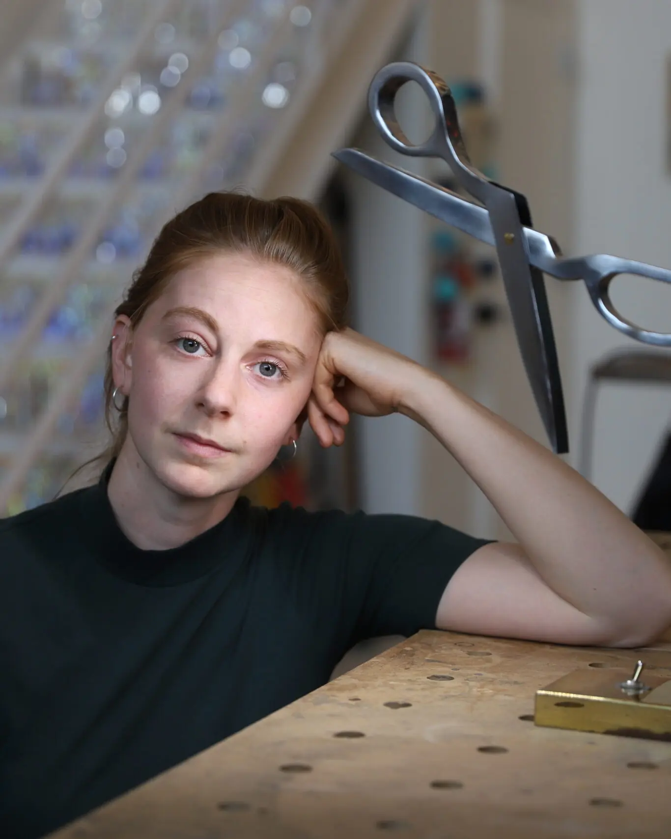 Simone Giertz leaning on her workbench beside a pair of giant scissors