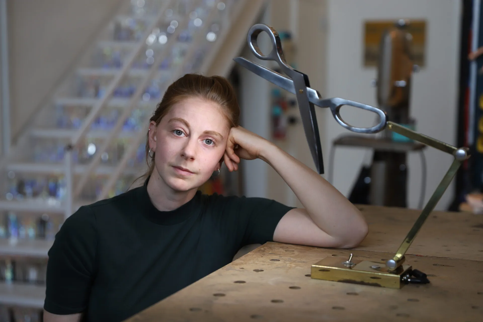 Simone Giertz leaning on her workbench beside a pair of giant scissors on a brass arm